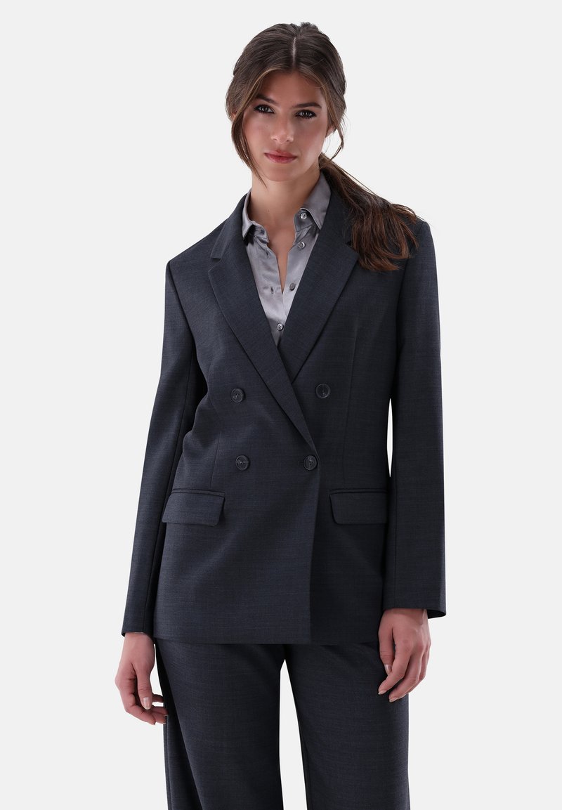 Dunkelgrauer doppelt geknöpfter Blazer mit Revers, zwei vorderen Taschen und glatter Textur, über einem hellgrauen Hemd mit Knopfleiste.