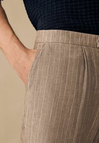 Pantalones de rayas finas en color marrón claro con un ajuste a medida, que cuentan con un bolsillo lateral y se combinan con una parte superior texturada en azul marino oscuro.