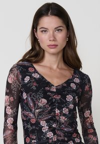 Top de manga larga negro con un patrón floral en tonos rosas y verdes, que presenta un escote en V y detalles fruncidos en la parte frontal.