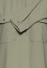 Hellgrünes Button-up-Hemd aus glattem Stoff, mit zwei Brusttaschen und umgeschlagenen Ärmeln. Einfaches Design mit modernem Abschluss.