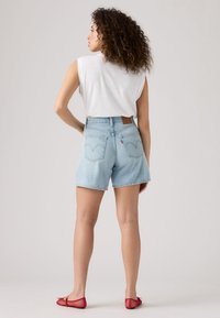 Lichtblauwe denim shorts met hoge taille, rechte pasvorm en rafelige zoom. Gecombineerd met een wit mouwloos topje en rode mesh ballerina's.