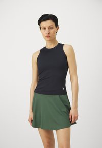 Navy ribbed tank top paired with a green flared skirt. The top has a round neckline and a small logo at the hem. Smooth fabric texture.
