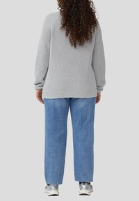 Grau strukturierter Strickpullover, lockere Passform, lange Ärmel; kombiniert mit hellblauen weit geschnittenen Jeans und silbernen Turnschuhen. Lässiges Outfit von hinten.