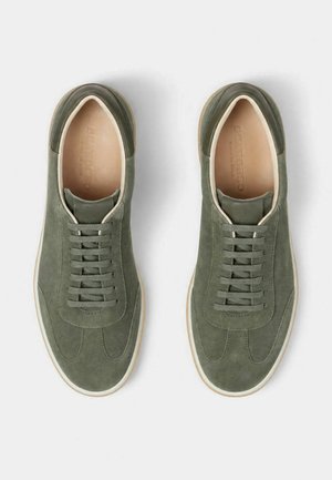 Paire de baskets en daim vert à lacets, doublure intérieure beige et semelles en caoutchouc blanches, vues de dessus sur fond blanc.