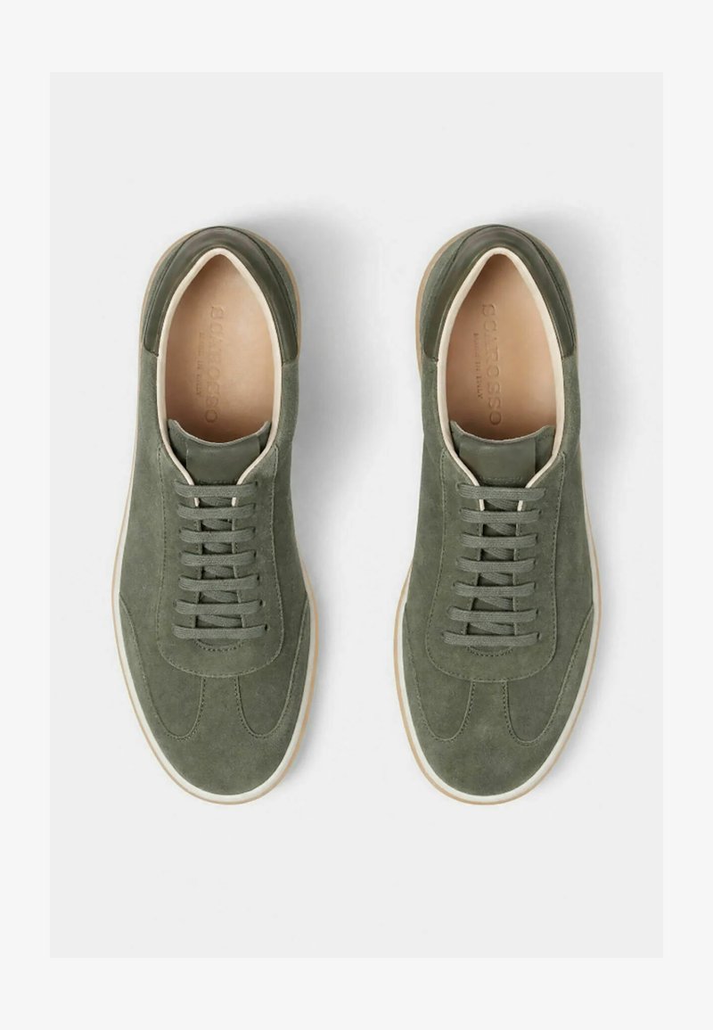 Paire de baskets en daim vert à lacets, doublure intérieure beige et semelles en caoutchouc blanches, vues de dessus sur fond blanc.