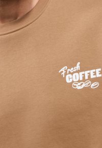 Sudadera marrón con cuello redondo que presenta un gráfico blanco "Fresh Coffee" y ilustraciones de granos de café, fabricada con un tejido suave y texturizado.