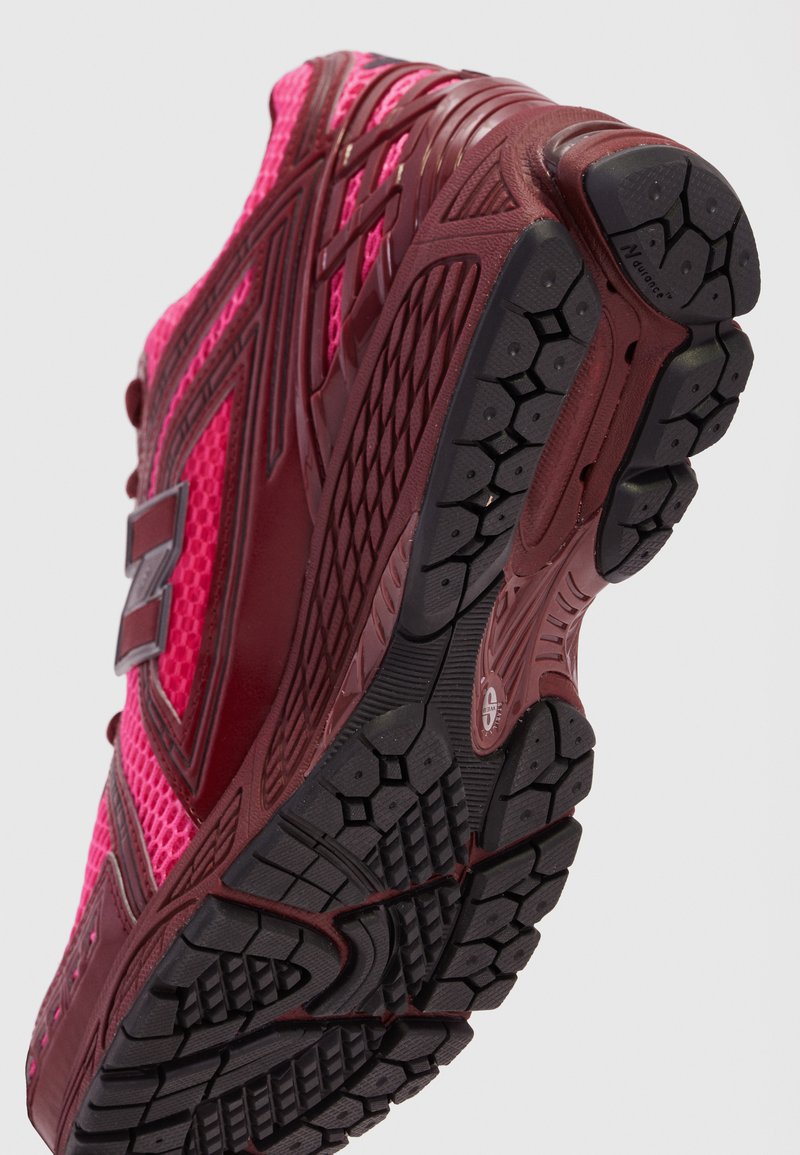 Athletic shoes with a mesh upper in bright pink, reinforced red accents, and a textured black rubber sole featuring a lug pattern for traction.