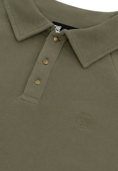 Olijfgroene polo met een kraag, drie decoratieve gouden knopen en een subtiele geborduurde logo op de borst.