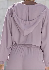 Ljuslila huvtröja med löst sittande passform, elastisk midja och långa ärmar. Mjuk textur och enkel designdetalj på baksidan.