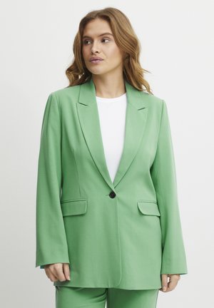 Zelený blazer se strukturovaným designem, jednořadovým zapínáním, klopovými límci a dvěma předními kapsami. Nosit s bílou košili.