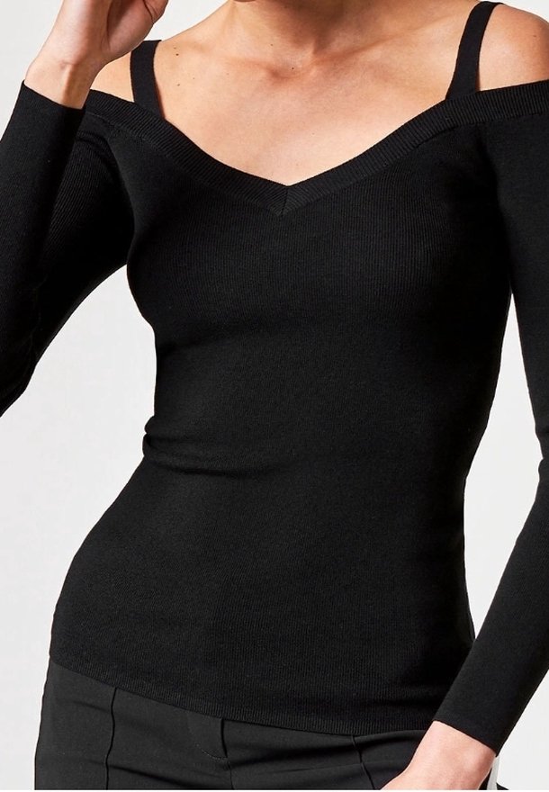 Haut noir en maille côtelée à manches longues avec découpes aux épaules et encolure en V profonde, porté avec un pantalon noir.