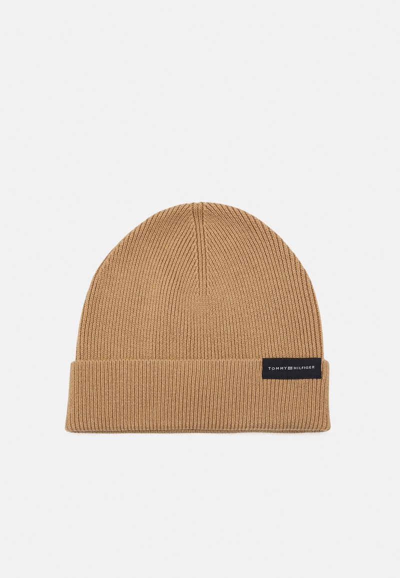 Bonnet en maille côtelée marron clair avec revers plié et petite étiquette noire portant l'inscription "Tommy Hilfiger" sur le devant du revers.