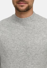 Maglione grigio a maglia con scollatura a girocollo a coste, caratterizzato da una texture morbida e un leggero motivo melange. Vista ravvicinata della parte superiore del corpo.