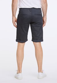 Pantaloni corti blu scuro realizzati in un tessuto texturizzato, con risvolti e tasche posteriori. Indossati con sneakers bianche.