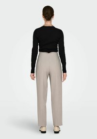 Haut noir à manches longues associé à un pantalon beige taille haute. La tenue présente une texture lisse et un design minimaliste.
