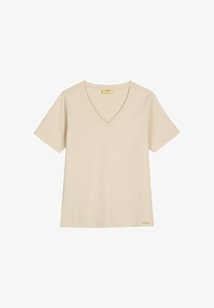 Beżowy T-shirt z krótkim rękawem i dekoltem w serek, z małą metką marki w pobliżu dolnego brzegu, ułożony płasko na białym tle.