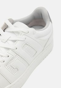 Hvite sneakers med glatt skinnutsiden, perforert design, snøring og grå detaljer ved hælen og kragen.