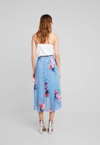 Gonna a pieghe di lunghezza media in azzurro chiaro con un motivo floreale in rosa e blu. Indossata con una canotta bianca e tacchi argentati.