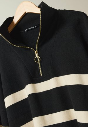 Schwarzer und cremefarbener gestreifter Strickpullover mit einem Reißverschlusskragen und goldenen Reißverschlussdetails. Der Stoff hat eine glatte Textur.