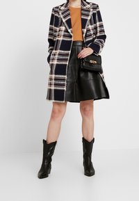 Ruudullinen takki laivastonsinisessä, viininpunaisessa ja kermanvärissä; musta nahkainen minihame; ruskea paita; musta käsilaukku; mustat cowboy-saappaat; sileät pinnat.