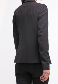 Černý ušitý blazer s přiléhavým střihem, hladkým materiálem, úzkými klopami a subtilním švem, z pohledu zezadu.