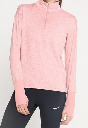Femme portant un haut de sport à manches longues rose clair avec des trous pour les pouces et des leggings noirs avec un logo Nike blanc.