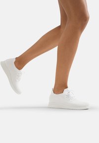 Sneakers bianchi in maglia con tomaia in tessuto, punta rotonda e suola piatta; presentano laccetti integrati e un tassello sul tallone.
