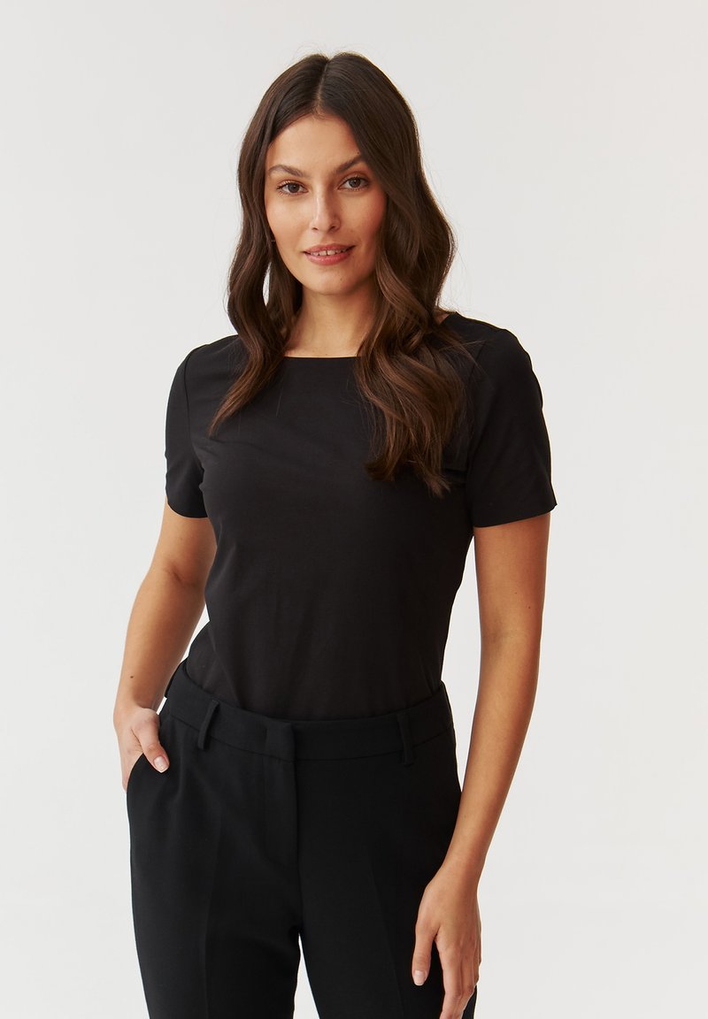 T-shirt noir à manches courtes avec un col carré, présentant une texture lisse, complété par un pantalon noir taille haute.
