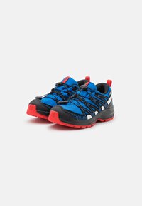 Zapatos de senderismo azul y negro con parte superior de malla texturizada, acentos rojos, cordones elásticos y suela negra resistente.
