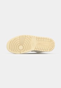 Egy Nike sneaker talpa, amely bézs árnyalatú mintás gumi textúrával rendelkezik, fehér háttér előtt.