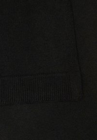 Gros plan sur un tissu tricoté noir présentant une texture côtelée sur le bord. Le matériau est lisse avec un motif uniforme sur l'ensemble.