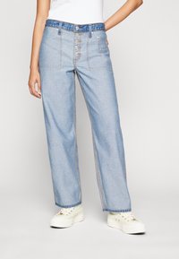 Jasnoniebieskie dżinsowe spodnie o szerokich nogawkach z guzikowym zapięciem, przednimi kieszeniami i kontrastującymi przeszyciami. W połączeniu z białymi sneakersami.