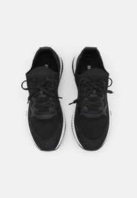 Svarta träningsskor har en ovandel av nät, platta snören och en texturerad sula. Designen inkluderar släta och perforerade paneler för ventilering.