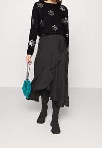 Czarny sweter z wzorem płatków śniegu, czarna warstwowa spódnica z falbankami, torba na sznurku w kolorze morskim oraz czarne kozaki za kolano.