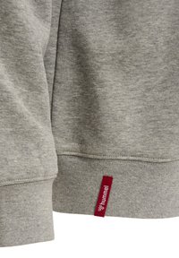 Grau Sweatshirtstoff mit einer glatten Textur, ausgestattet mit einem roten Etikett, das am Saum angenäht ist und den Markennamen "hummel" zeigt.