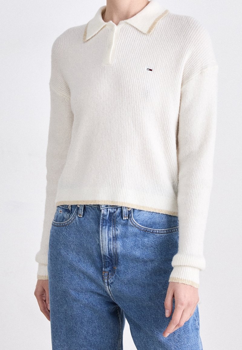 Pull polo en maille côtelée crème à manches longues avec finition beige, associé à un jean en denim bleu taille haute.