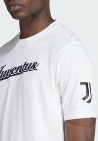 White cotton t-shirt with black embroidered "Juventus" text on the front and a black logo on the left sleeve; short sleeves, standard fit.