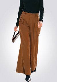 Bruine wijde broek met plooien aan de voorkant, hoge taille en een gladde textuur, gecombineerd met een zwart topje en een zwarte handtas.