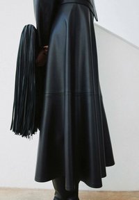 Zwarte leren rok met een vloeiende silhouet, voorzien van een gladde textuur en subtiele naden. Een franjesaccessoire complementeert de outfit.