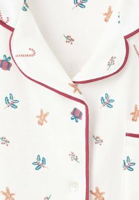 Pamučna pidžama gornji dio s bijelom pozadinom, s raznobojnim uzorcima vezanim za blagdane poput čovječuljaka od medenjaka, bobica i štapića od šećera. Bordo obrub.