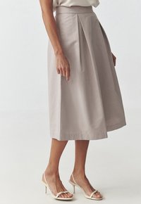 Jupe midi évasée taille haute beige avec pli avant, portée avec un haut sans manches blanc et des sandales à talons avec bride arrière crème.