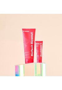 To røde rør med hårbehandling, ett stort og ett lite, vist på en klar, reflekterende blokk. Designet har hvit tekst og detaljer.