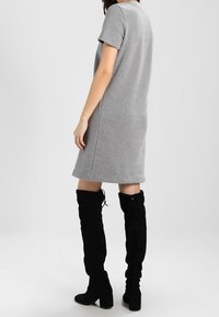 Grå kortärmad klänning i mjukt material, med avslappnad passform och rak nederkant. Kombinerad med höga svarta stövlar i mocka med snörningsdetaljer.