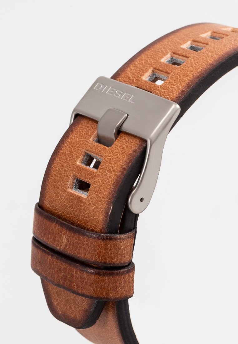 Bracelet de montre en cuir marron avec une finition texturée, comportant des trous découpés et une boucle en métal argenté portant le nom de la marque "DIESEL".