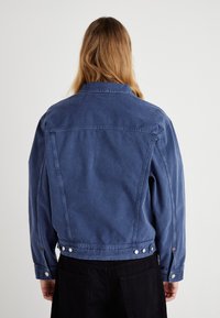 Jeansjacka i en bleknad blå färg, med klassisk krage, långa ärmar och silverfärgade tryckknappar längs midjan och ärmsluten.