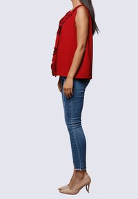 Top rojo sin mangas con detalle de volantes en el costado, combinado con jeans ajustados azules y tacones nude. Textura suave, ajuste casual.