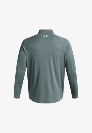 Långärmad, kragskjorta i texturerat grönt tyg. Har en rund logotyp nära kragen och en böjd fåll längst ner.