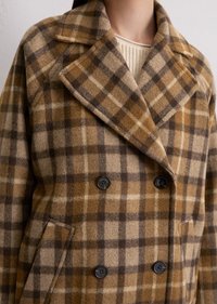 Dubbelgestreepte wollen jas met een bruin en beige ruitpatroon, grote revers en zwarte knopen. Textiel met structuur, warme stof.