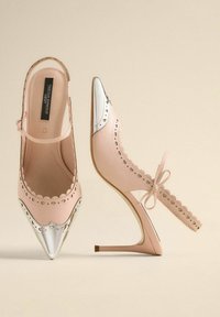 Scarpe con tacco alto rosa, con punta affusolata, cappuccio metallico argento, bordi ripiegati, ritagli a forma di cuore e cinturino alla caviglia con dettaglio a fiocco.