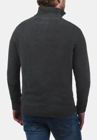 Suéter de punto en carbón con un alto cuello acanalado, acabado texturizado y puños acanalados. Ajuste entallado, combinado con jeans azules.